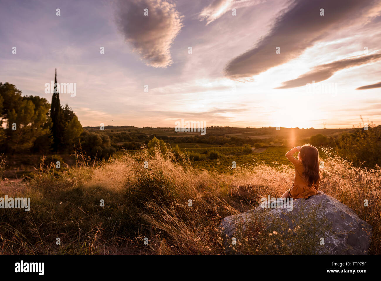 Ragazza seduta sulla roccia si affaccia sulla vallata al tramonto le nuvole in cielo Foto Stock