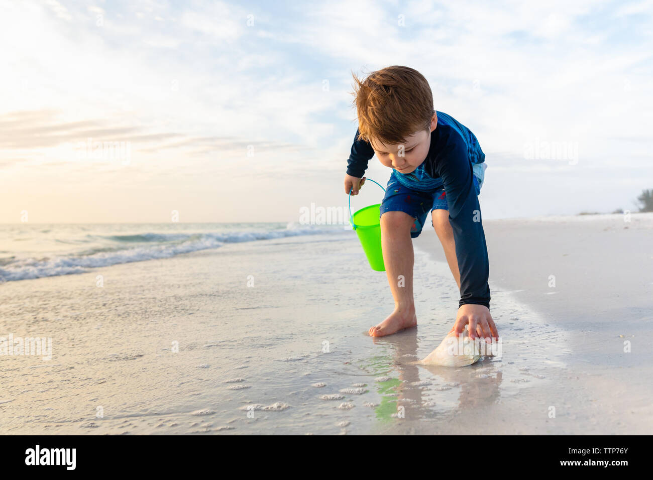 Bambino chinarsi per raccogliere conchiglie sulla spiaggia Foto Stock
