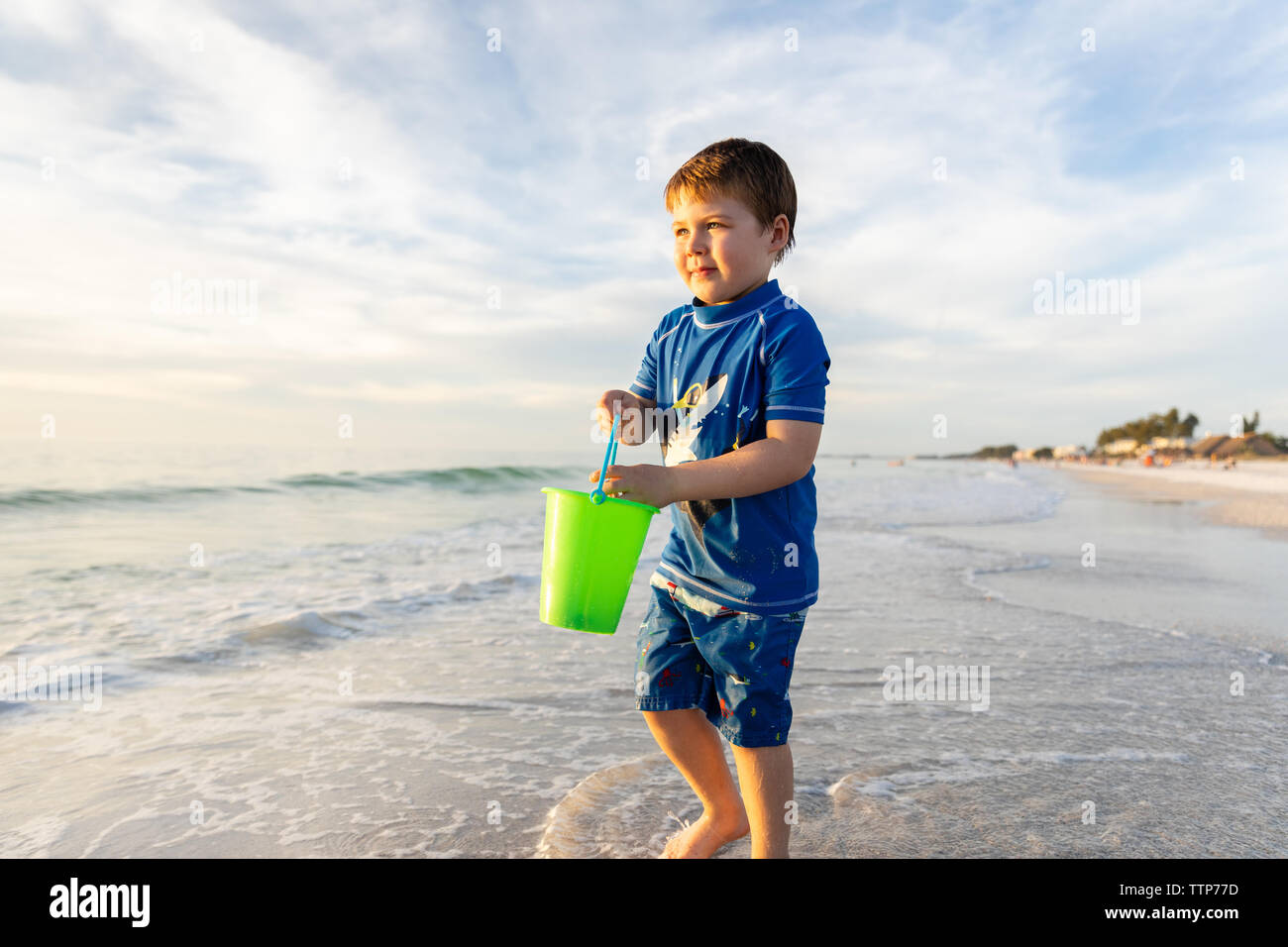 Ragazzo guarda con speranza alla ricerca di conchiglie sulla spiaggia Foto Stock