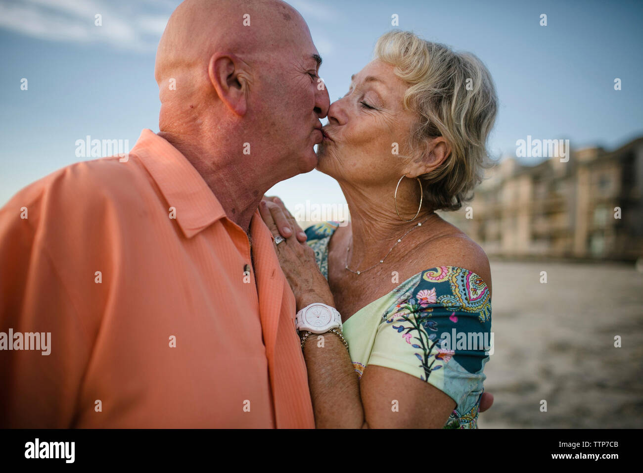 Romantico coppia senior kissing mentre si sta in piedi in spiaggia contro sky Foto Stock