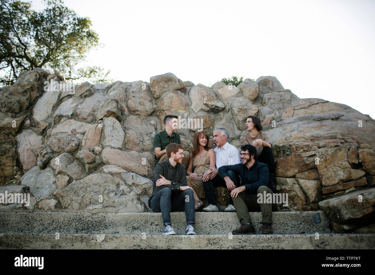 La famiglia felice di parlare mentre è seduto da formazioni rocciose contro il cielo chiaro al park Foto Stock