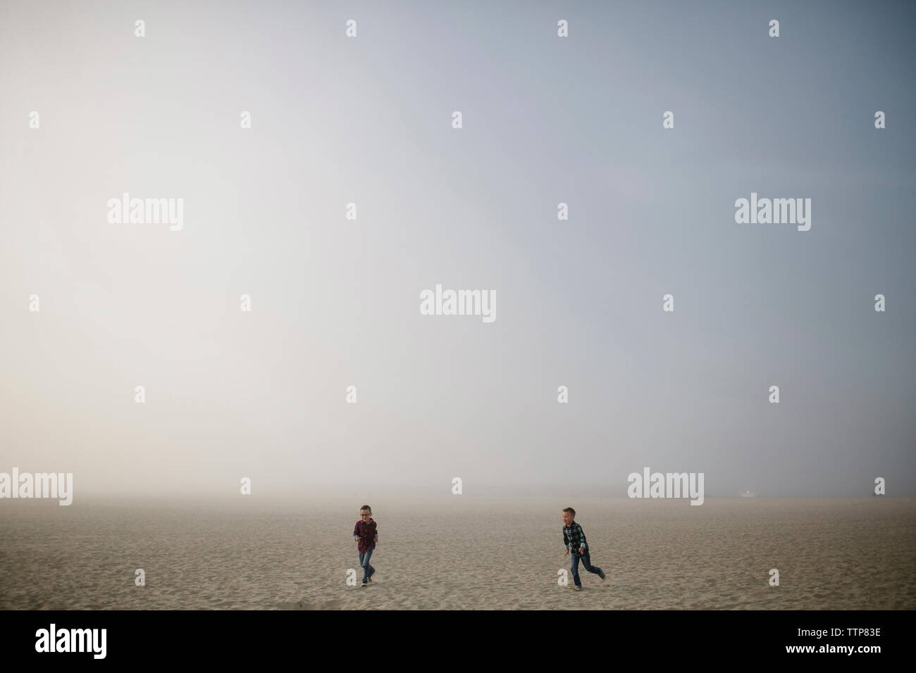 Giocoso fratelli in esecuzione sulla sabbia in spiaggia contro il cielo durante la nebbia meteo Foto Stock