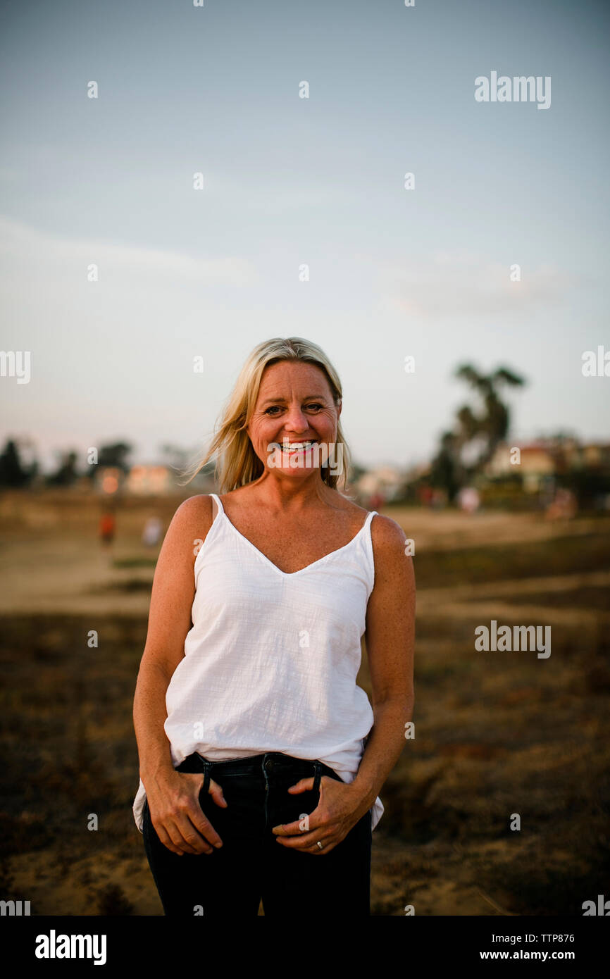 Ritratto di donna felice in posa mentre si sta in piedi sul dirupo contro il cielo durante il tramonto Foto Stock