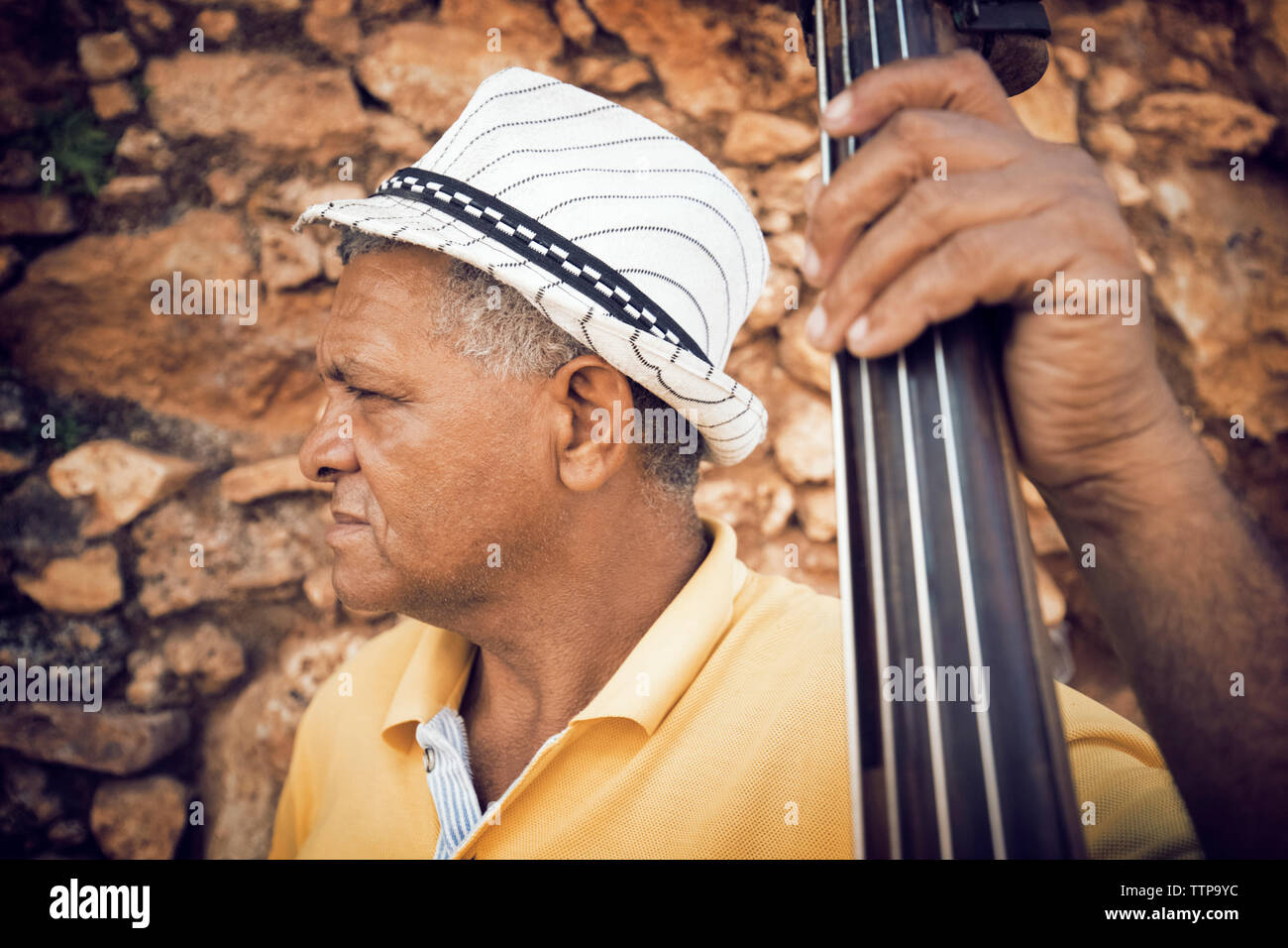 Close-up di uomo con contrabbasso mentre in piedi contro il muro di pietra Foto Stock