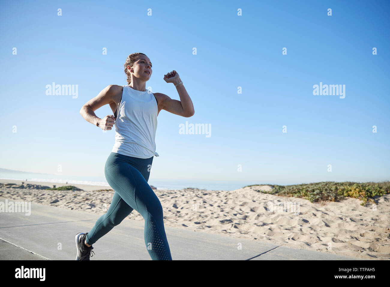 Donna jogging sulla strada dalla spiaggia contro il cielo chiaro Foto Stock