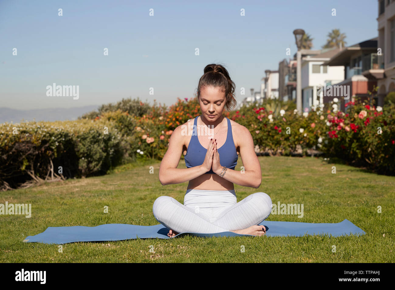 Donna con le mani incrociate e a gambe incrociate meditando sul tappeto di esercizio Foto Stock