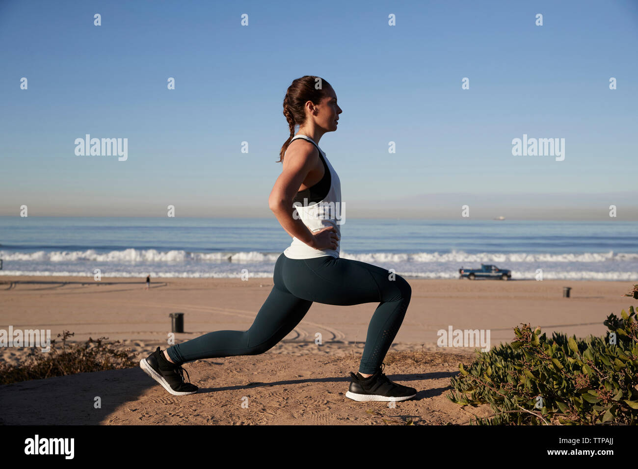 Vista laterale della donna con le mani sul hip stretching contro il cielo chiaro a beach Foto Stock