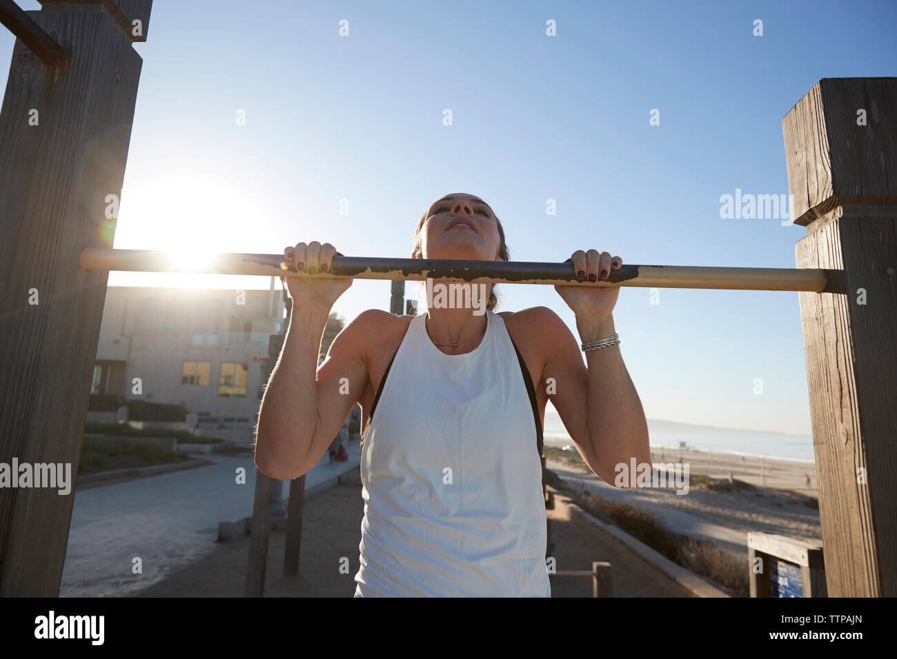 Donna facendo chin-ups sulla barra di ginnastica in spiaggia durante il giorno di sole Foto Stock