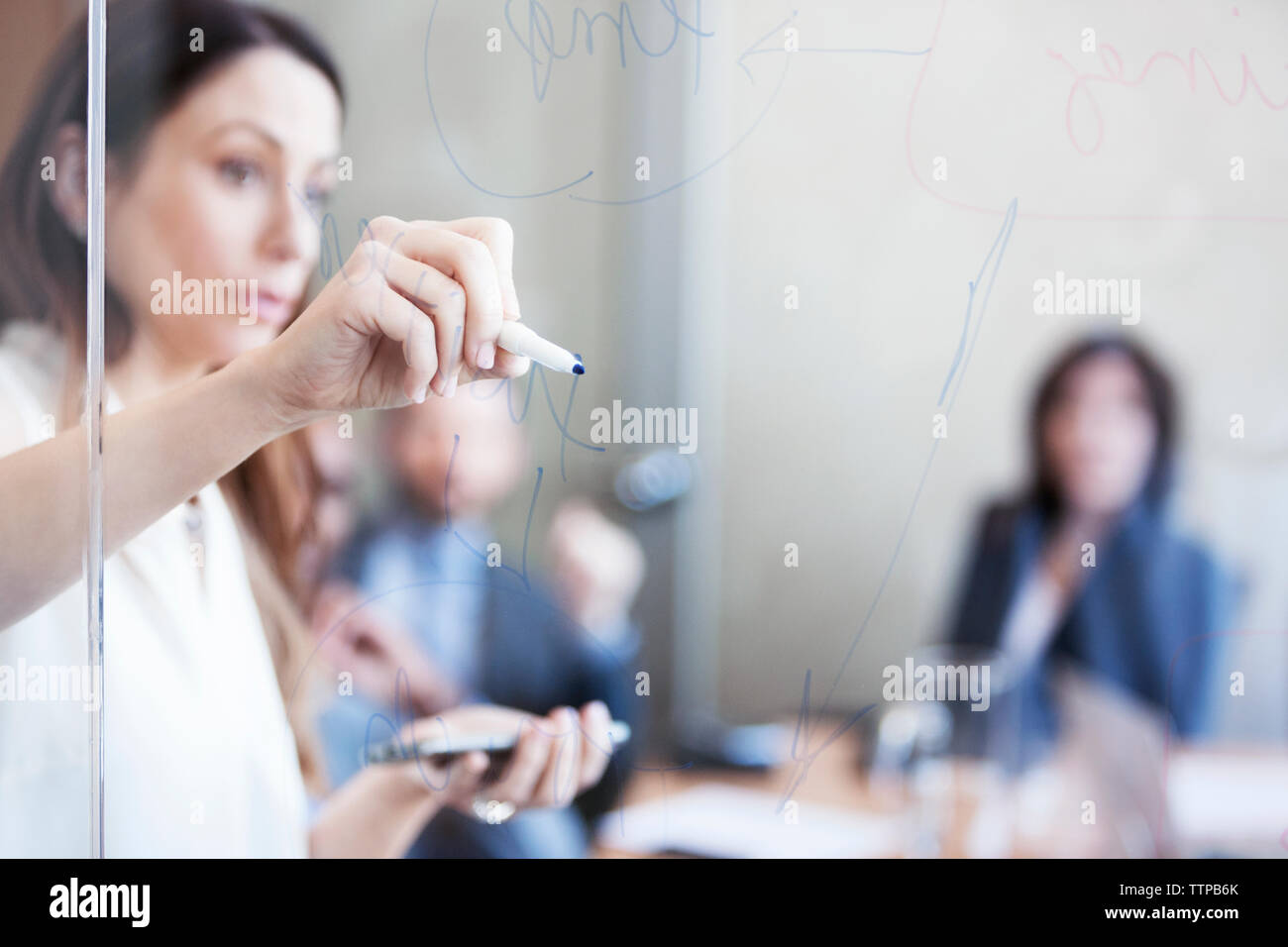 donna d'affari che scrive su una parete di vetro durante la riunione Foto Stock