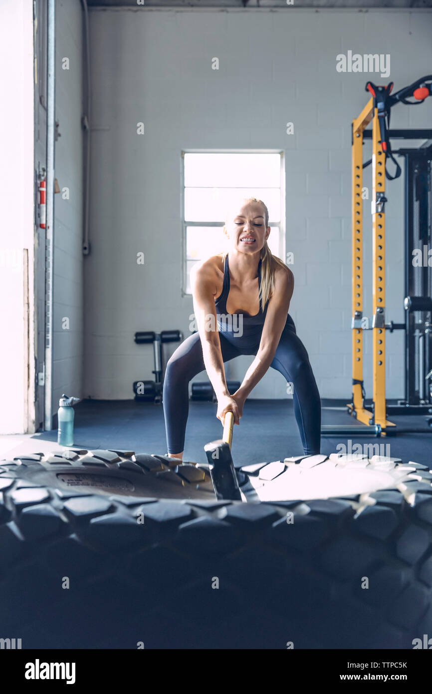Determinata donna colpendo pneumatico con mazza mentre ti alleni in palestra Foto Stock