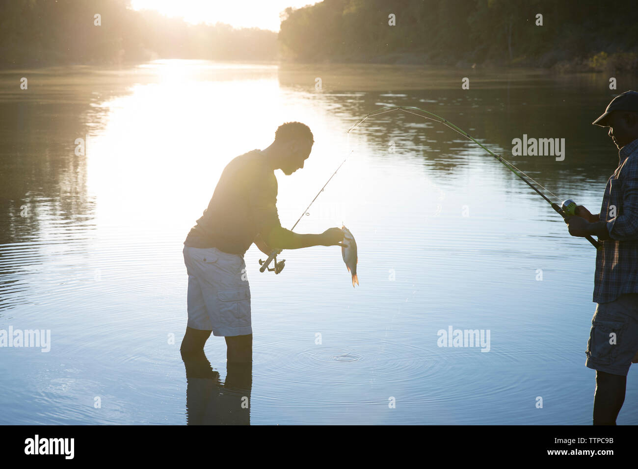 Vista laterale dei maschi di amici di pesca in lago durante il tramonto Foto Stock