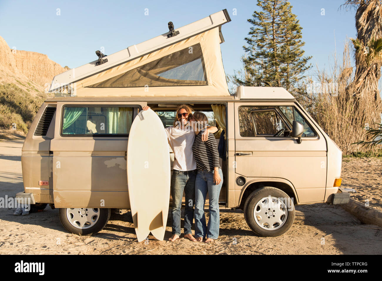 Amare donna baciare uomo con la tavola da surf di contenimento nella parte anteriore del mini van su San Onofre State Beach Foto Stock