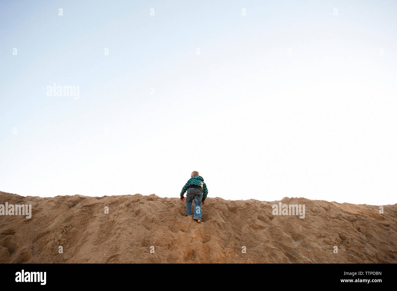 Vista posteriore del ragazzo arrampicate sulle dune di sabbia in spiaggia contro sky Foto Stock