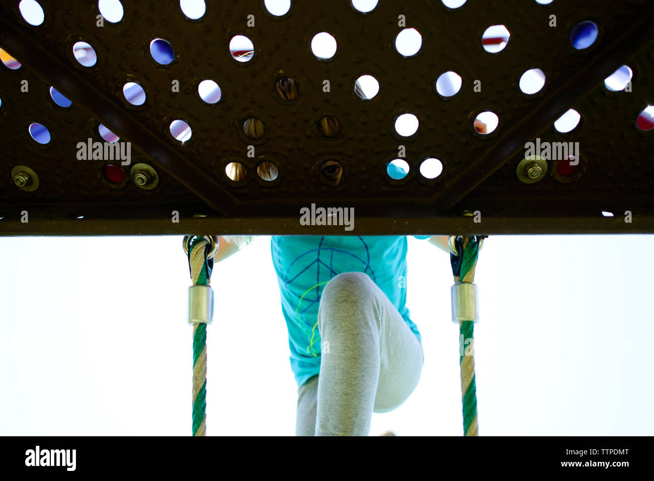 Basso angolo vista della ragazza spiata attraverso il foro mentre alpinismo scaletta di corda e al parco giochi Foto Stock