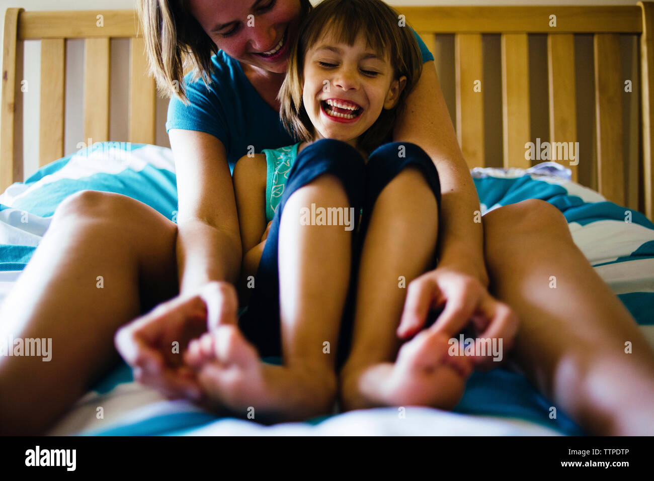 Felice madre figlia solletica i piedi mentre si siede sul letto Foto Stock