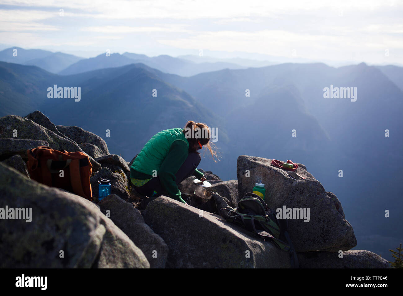 Escursionista acqua bollente mentre accovacciato sulle rocce contro le montagne Foto Stock