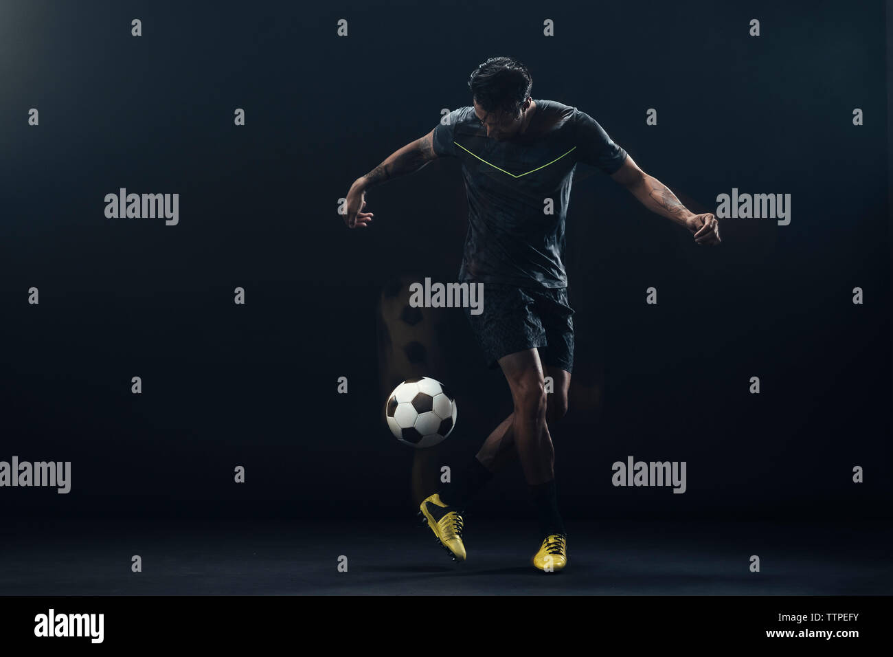 Lunghezza completa di giocatore di calcio calci palla contro lo sfondo nero Foto Stock
