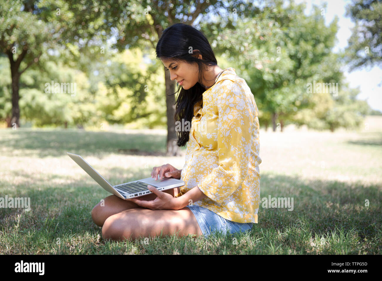 Donna sorridente con notebook seduti su erba a park Foto Stock