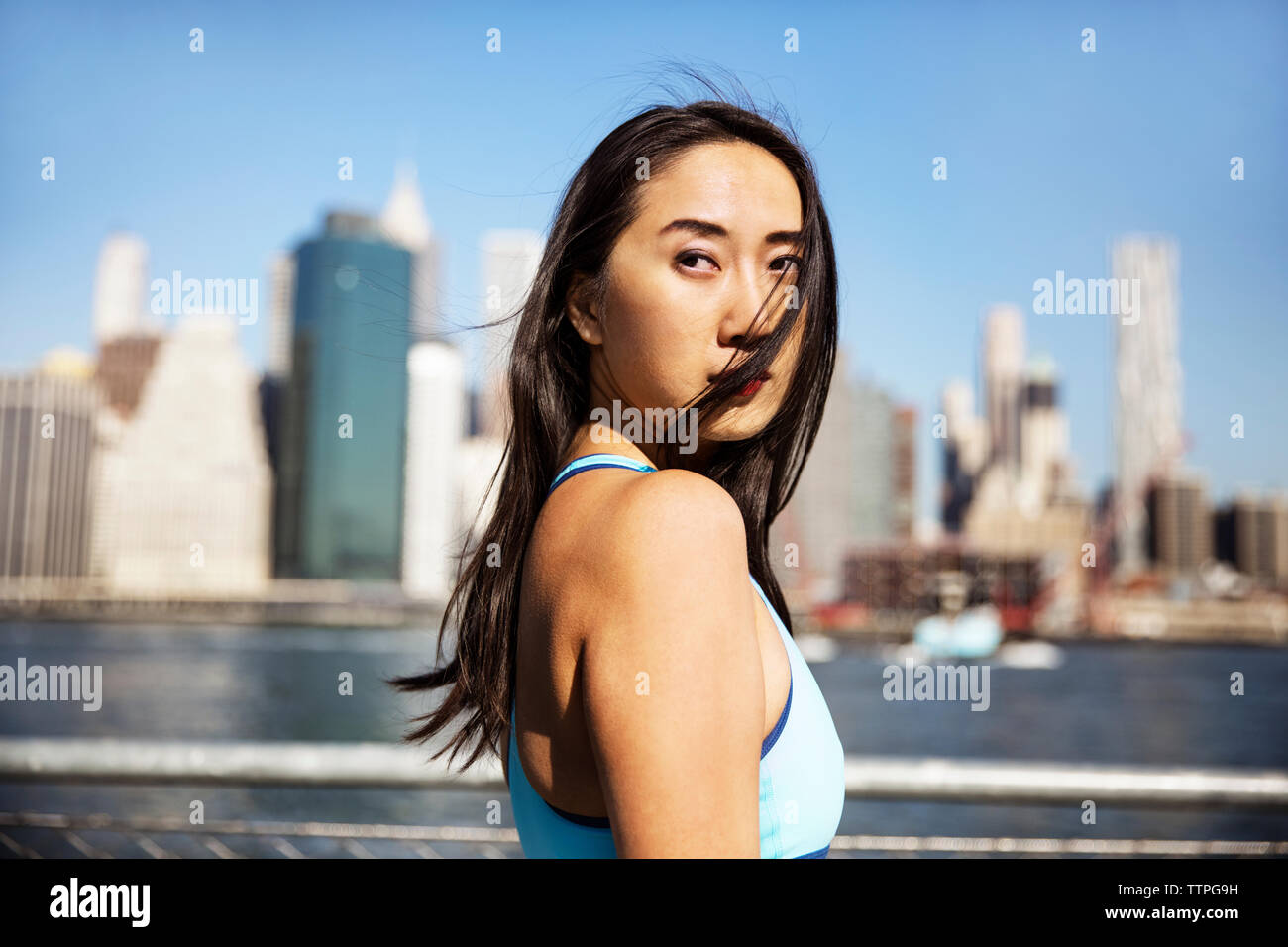 Vista laterale di pensosa atleta femminile in piedi contro lo skyline della città Foto Stock