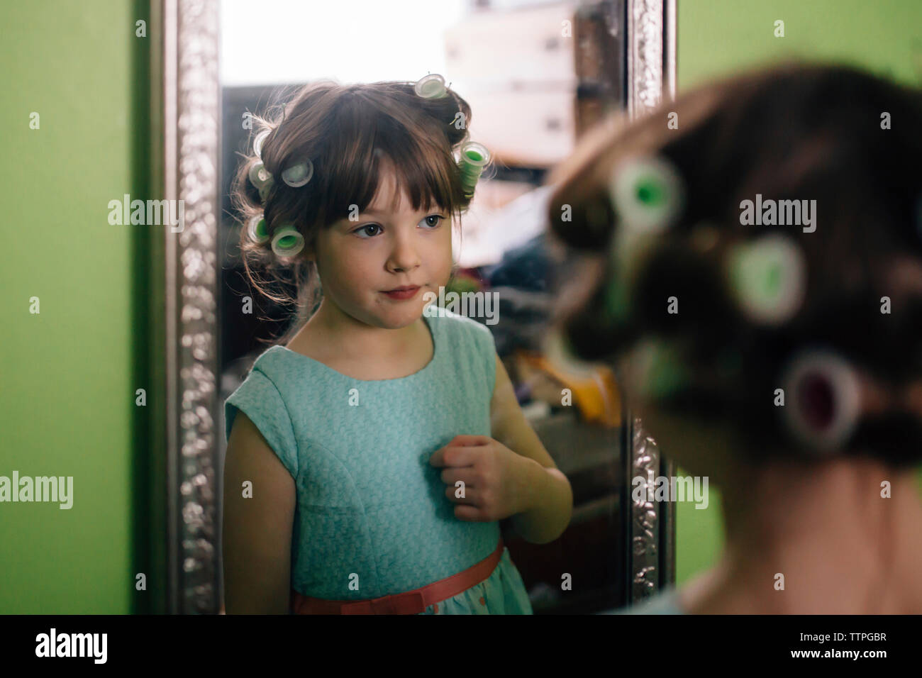 Ragazza con arricciacapelli riflettendo sullo specchio mentre sta in piedi a casa Foto Stock