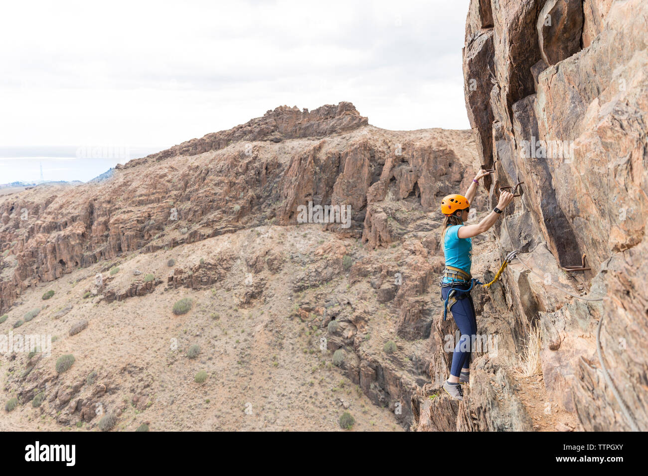 Escursionista femmina utilizzando i pioli durante la salita sulla formazione di roccia Foto Stock