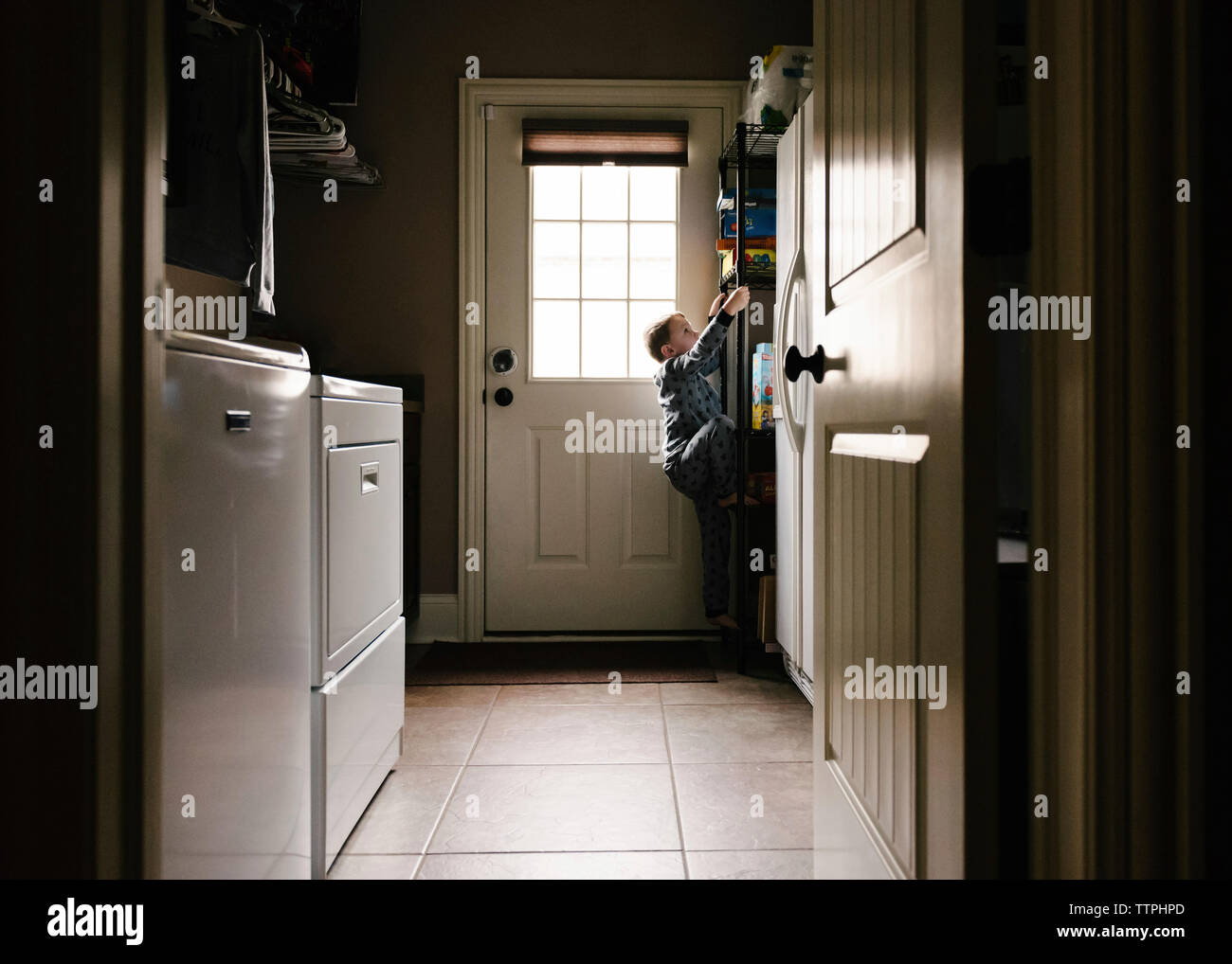 Vista laterale del ragazzino spensierato arrampicata su rack a casa visto attraverso la porta Foto Stock