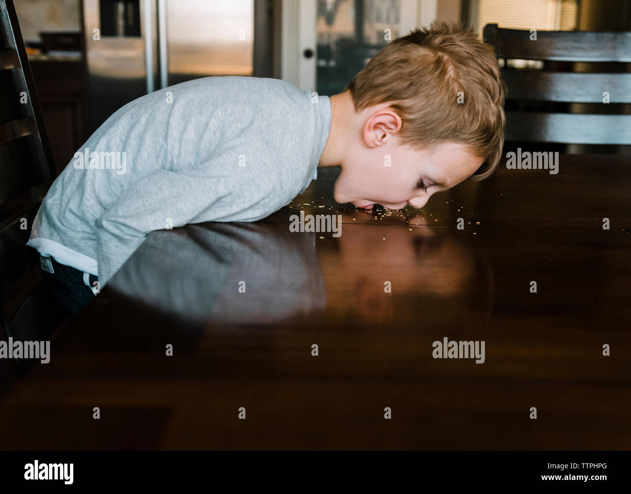 Giocoso ragazzo leccare il cibo dalla tabella a casa Foto Stock