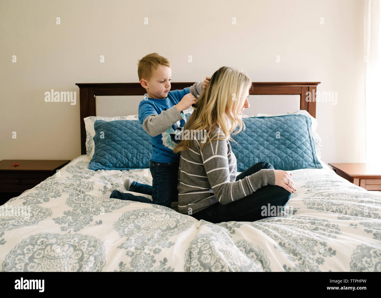 Carino figlio di madre di pettinatura dei capelli mentre inginocchiato sul letto contro la parete a casa Foto Stock