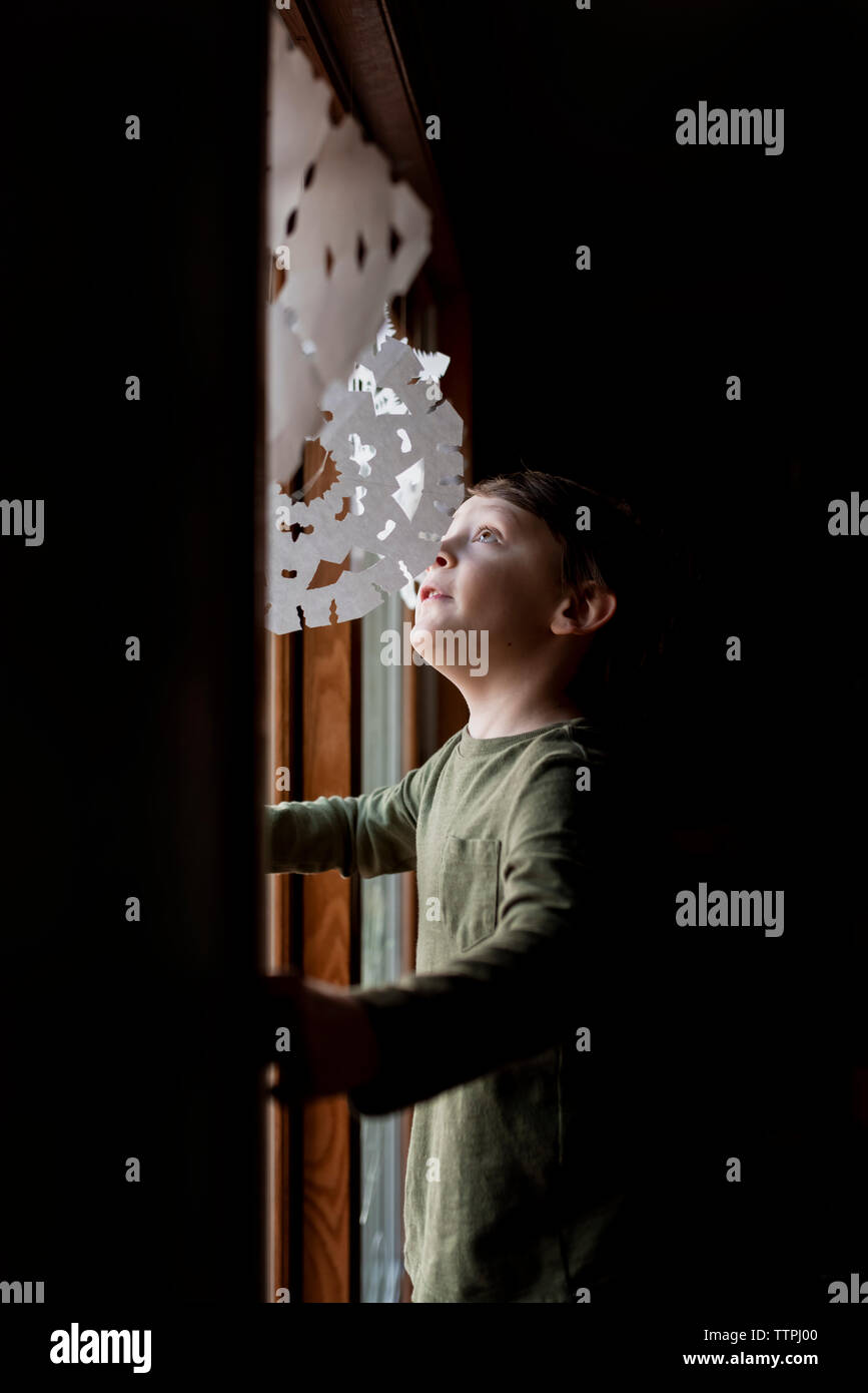 Un piccolo ragazzo alla ricerca fino a carta fiocchi di neve in una finestra Foto Stock