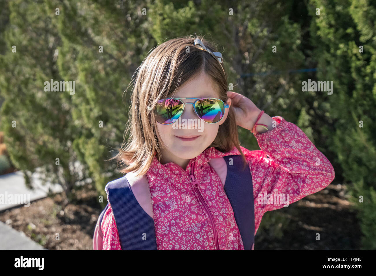 Close-up ritratto di ragazza con zaino indossando occhiali da sole mentre in piedi contro piante durante la giornata di sole Foto Stock