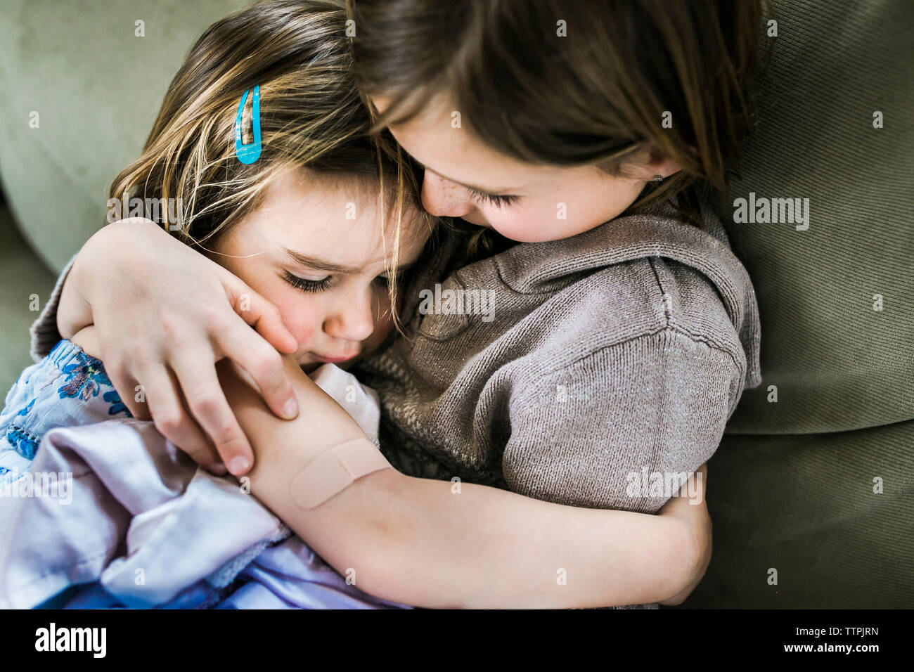 Angolo di Alta Vista della ragazza abbracciando la sorella comodamente seduti sul divano di casa Foto Stock