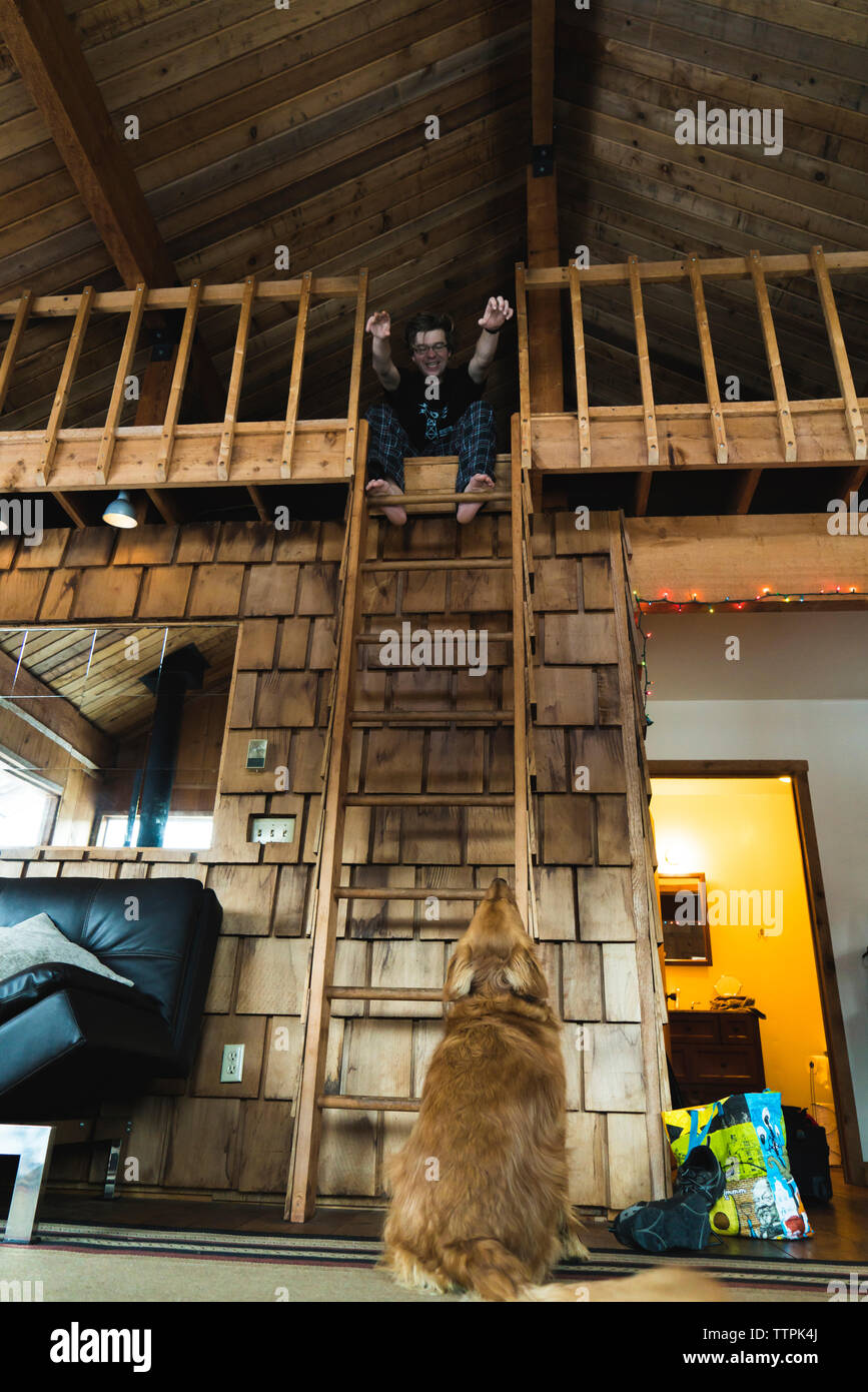Vista posteriore del Golden Retriever guardando uomo seduto su attico in cottage Foto Stock