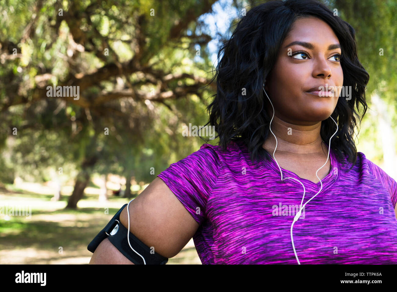 Fiducioso donna che guarda lontano mentre si ascolta la musica al parco Foto Stock