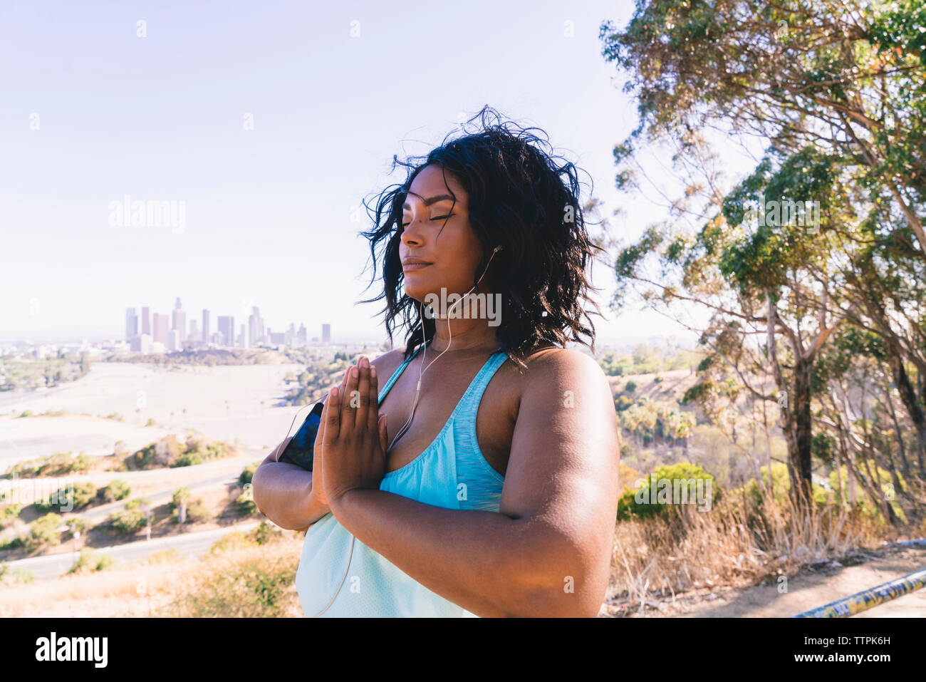 Donna con gli occhi chiusi facendo posizione di preghiera esercitare contro il cielo chiaro Foto Stock