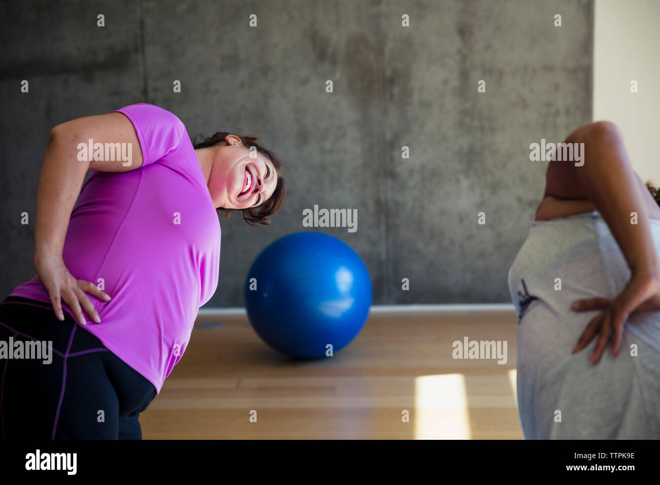 Happy amici di sesso femminile con le mani sui fianchi la piegatura durante l esercizio faccia a faccia in studio di yoga Foto Stock