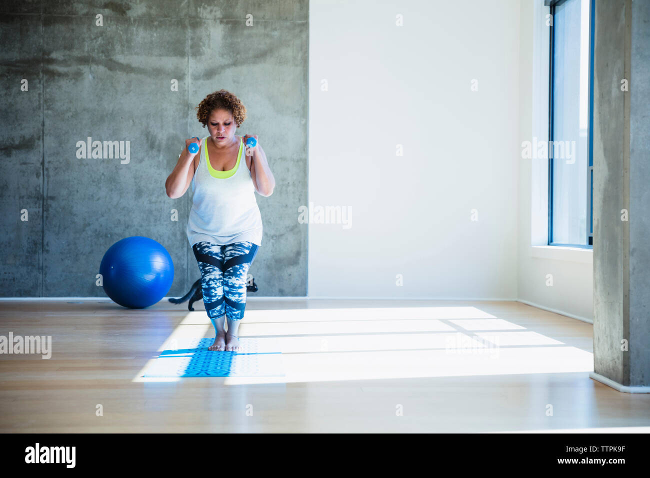 Focalizzato donna esercizio mentre utilizzando pesi contro la parete in studio di yoga Foto Stock