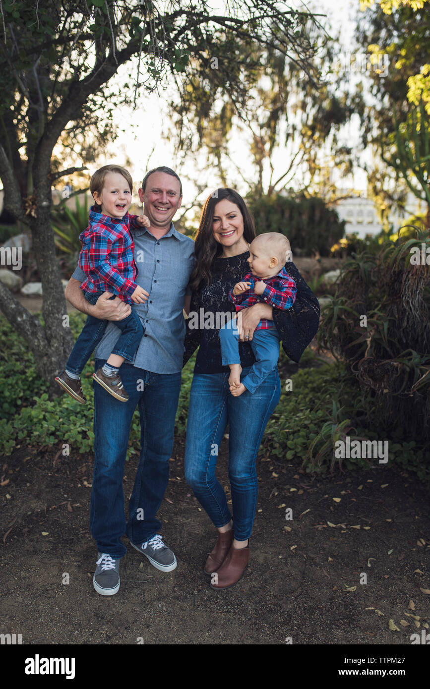 Ritratto di genitori felici che trasportano figli rimanendo in posizione di parcheggio Foto Stock