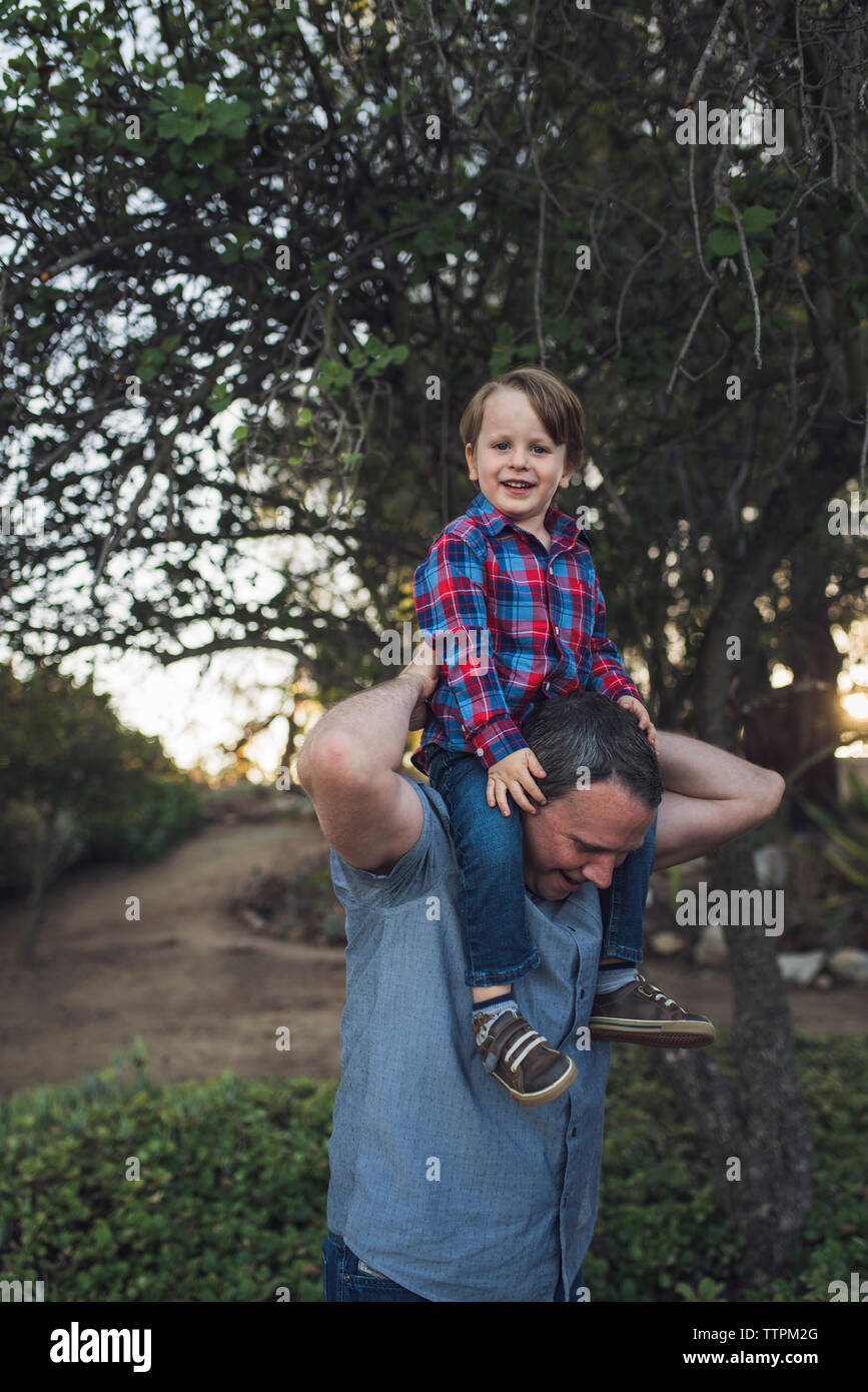 Ritratto di sorridere Figlio seduto sul padre di spalle mentre giocando a park Foto Stock