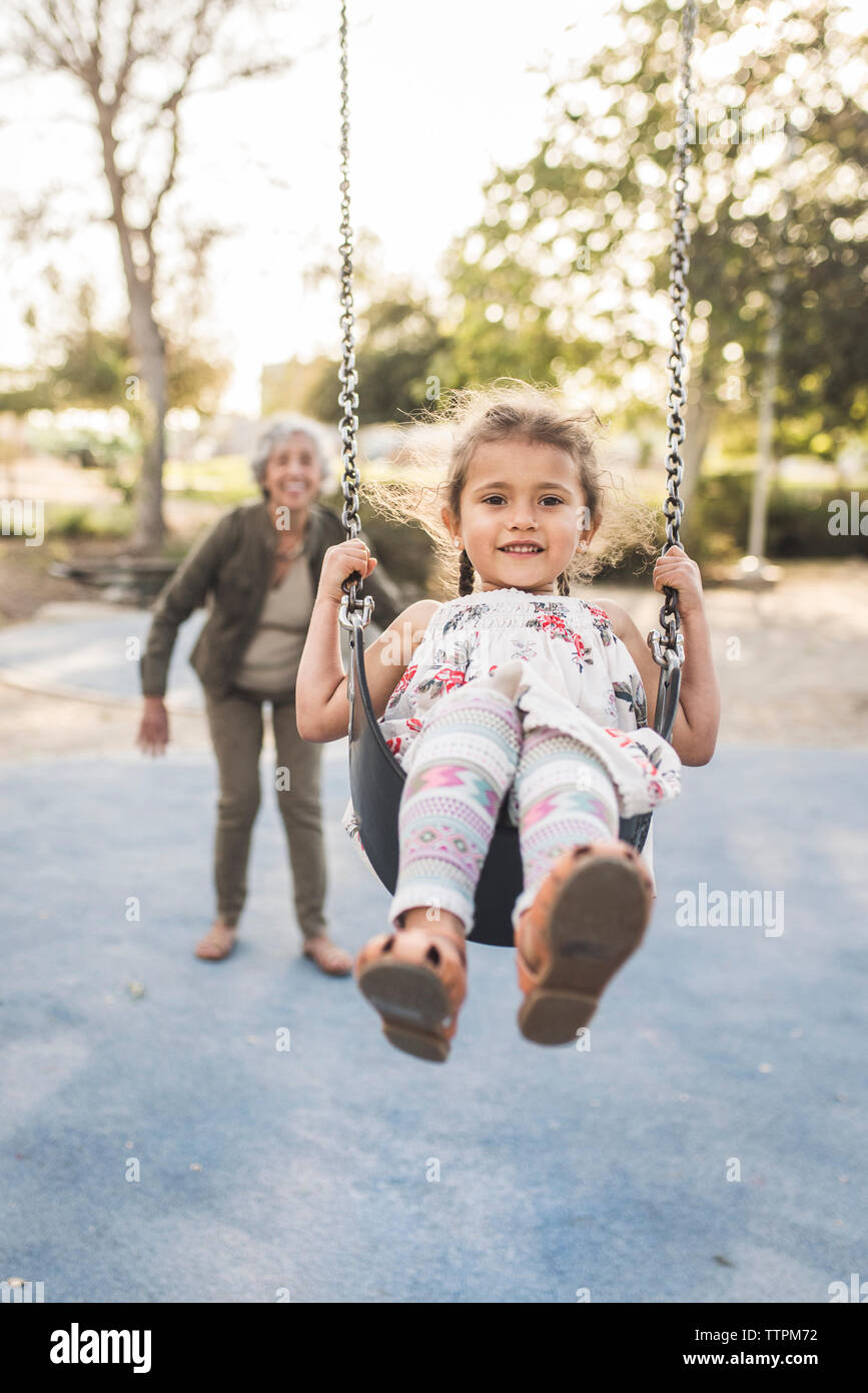 Nonna felice spingendo la nipote swinging presso il parco giochi Foto Stock