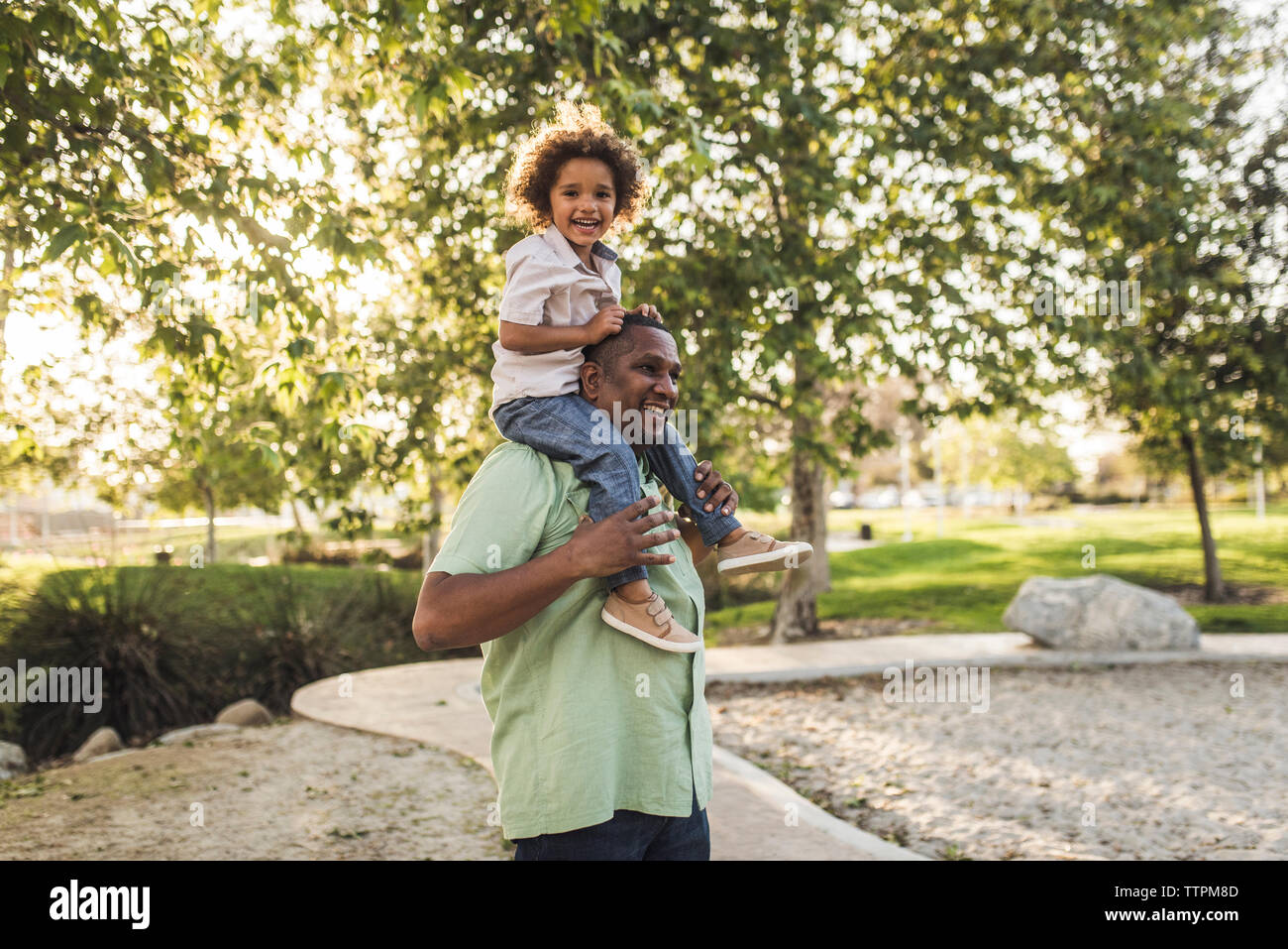 Ritratto di Allegro Figlio seduto sul padre di spalle mentre giocando a park Foto Stock