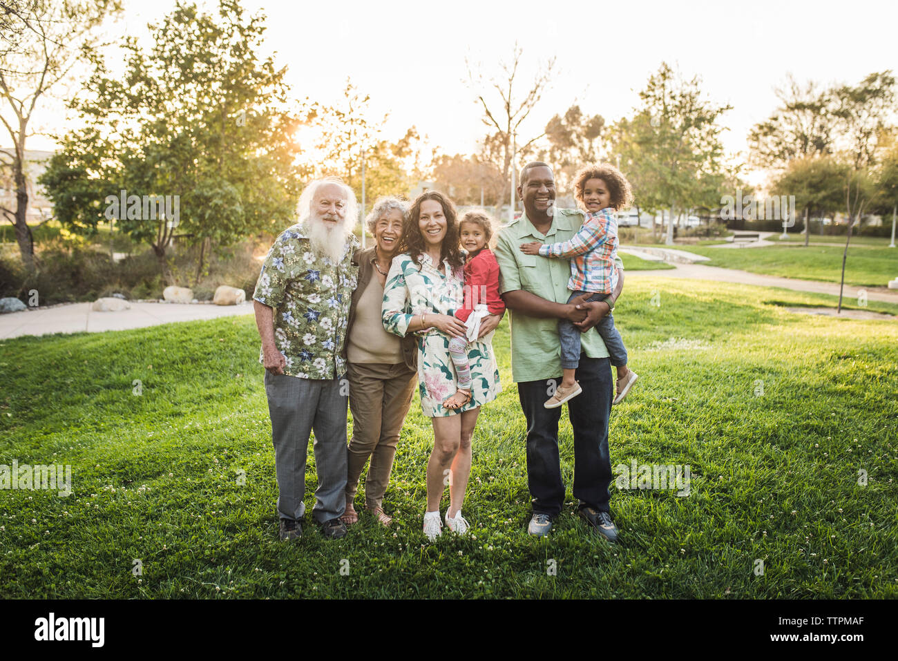 Ritratto di felice multi-famiglia di generazione in piedi sul campo erboso a park Foto Stock