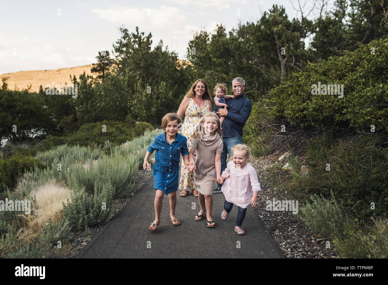 Genitori felici guardando le figlie tenendo le mani mentre si cammina sulla strada contro gli alberi nelle foreste Foto Stock