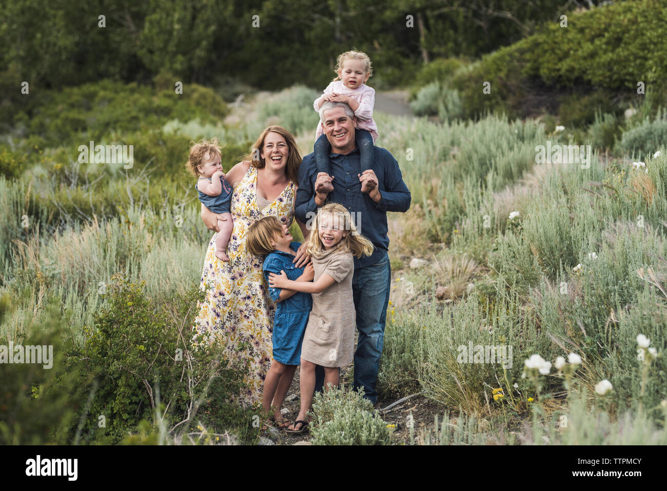 Ritratto di genitori felici con graziosi figlie in piedi sul campo nel mezzo di piante in foresta Foto Stock