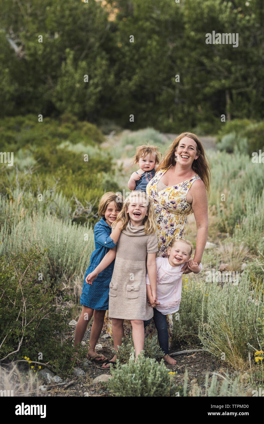 Ritratto di felice madre con graziosi figlie in piedi sul campo nel mezzo di piante in foresta Foto Stock