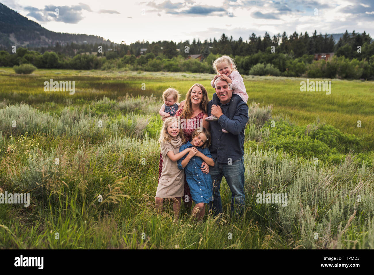 Ritratto di genitori felici con graziosi figlie in piedi sul campo erboso contro sky in foresta Foto Stock