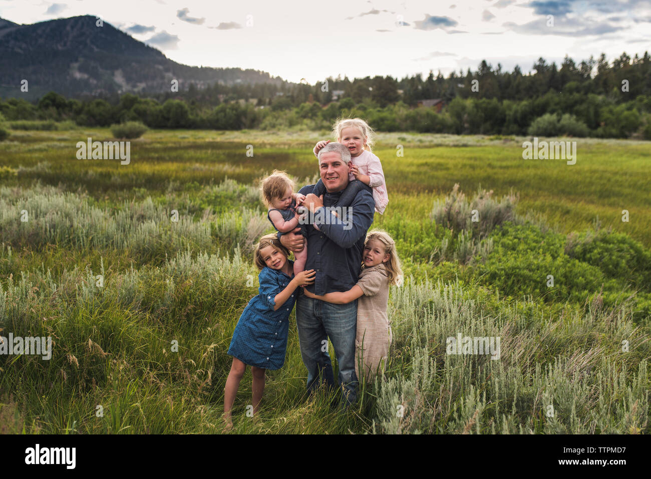Ritratto di padre con graziosi figlie in piedi sul campo erboso contro sky in foresta Foto Stock