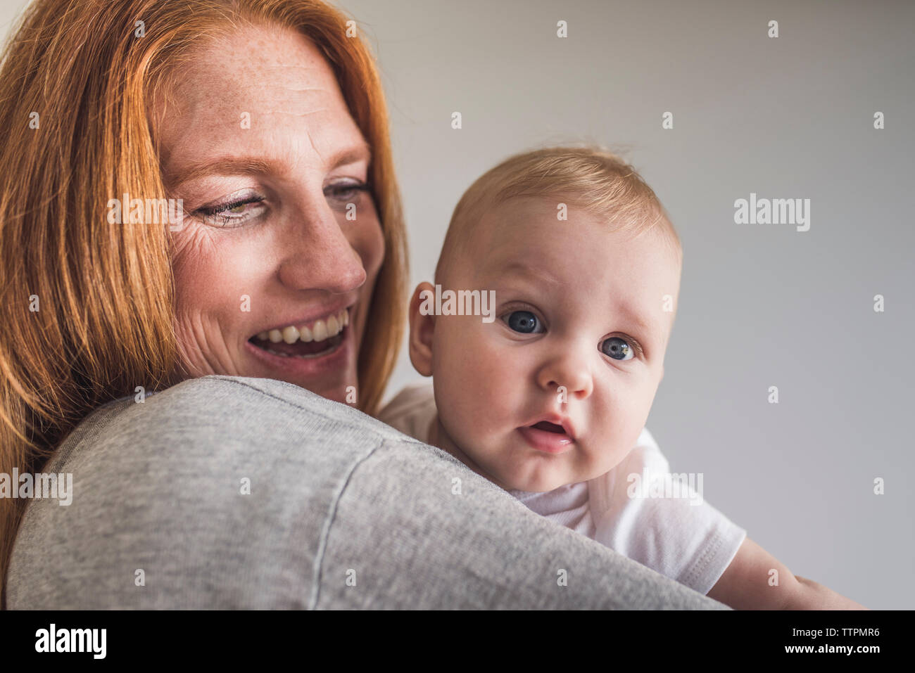Close-up di felice madre che trasportano carino figlio mentre in piedi contro il muro grigio a casa Foto Stock