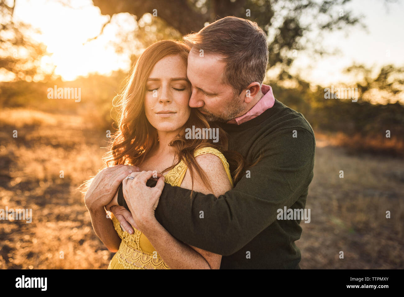 Il marito abbracciando la moglie mentre nel campo della California durante il tramonto Foto Stock