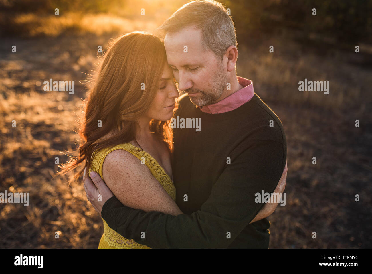 Donna abbracciando il marito mentre nel campo della California durante il tramonto Foto Stock
