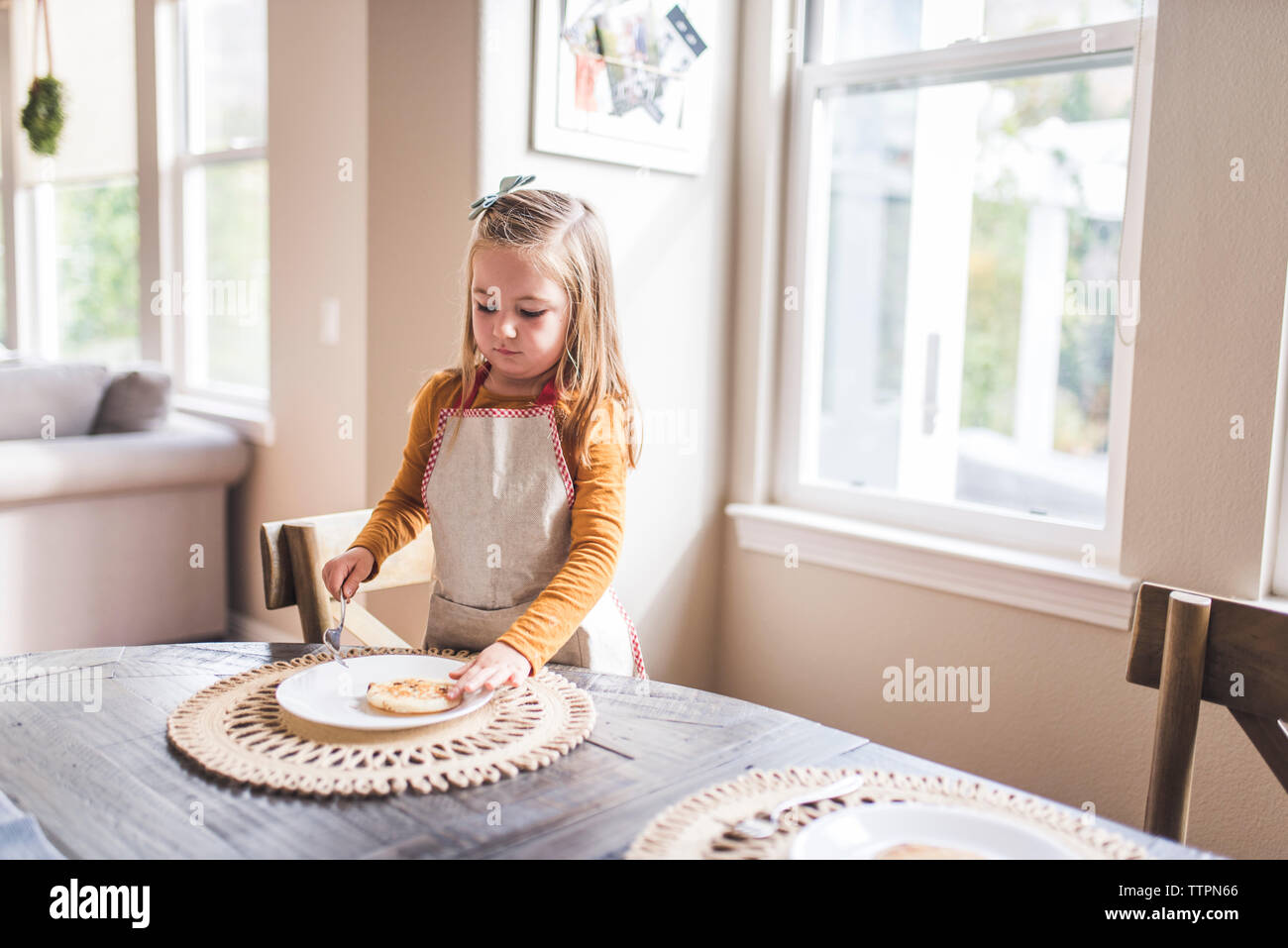 Bambina con grembiule flipping pancake al tavolo per la colazione Foto Stock